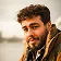 A man with a beard wearing a brown jacket stands confidently